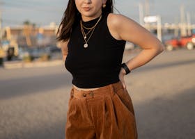 Woman in black crop top and brown pants posing outdoors at sunset.